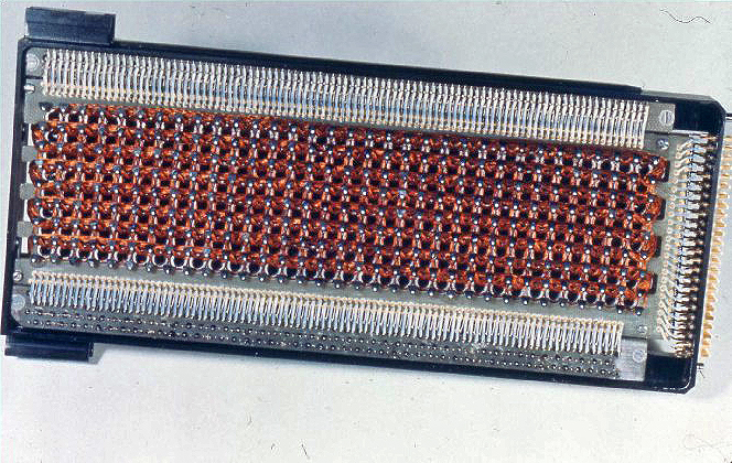 This is a photograph of a segment of the Apollo Guidance Computer's Core Rope Memory. Many copper wires are arranged in a roughly grid-like pattern in the center of the image. Around the outside of the copper grid, silver connectors are arranged in tight vertical lines. The entire assembly is bordered by a black rectangular enclosure about twice as wide as it is tall.